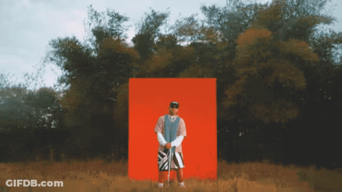 A Man Is Standing In Front Of A Red Box In A Field GIF