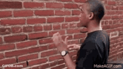 A Man Is Standing In Front Of A Red Brick Wall . GIF
