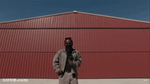 A Man Is Standing In Front Of A Red Building That Says Vevo On The Bottom Right GIF