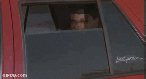 A Man Is Standing In Front Of A Red Car Holding A Plate . GIF