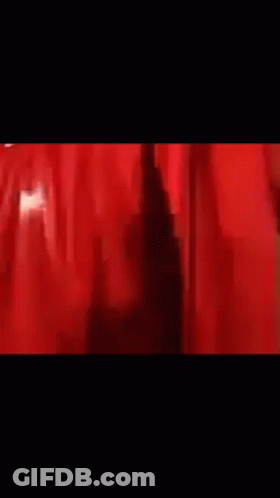 A Man Is Standing In Front Of A Red Curtain In A Dark Room . GIF