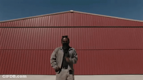 A Man Is Standing In Front Of A Red Wall GIF