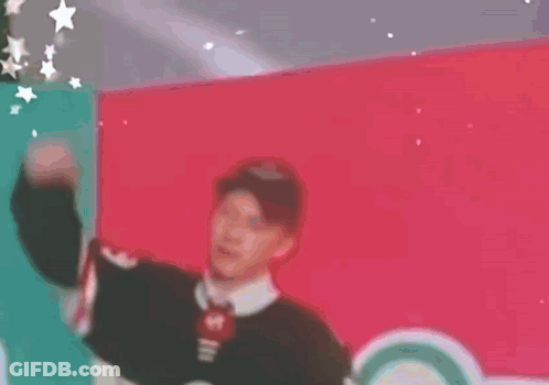 A Man Is Standing In Front Of A Red Wall And Making A Funny Face . GIF
