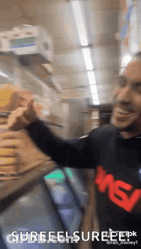 A Man Is Standing In Front Of A Refrigerator In A Store And Giving A Thumbs Up . GIF