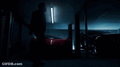 A Man Is Standing In Front Of A Row Of Cars In A Dark Garage GIF