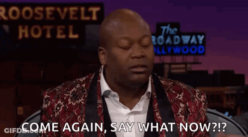 A Man Is Standing In Front Of A Sign That Says `` Come Again , Say What Now ? '' . GIF
