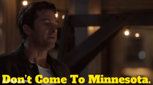 A Man Is Standing In Front Of A Sign That Says " Don 'T Come To Minnesota " GIF