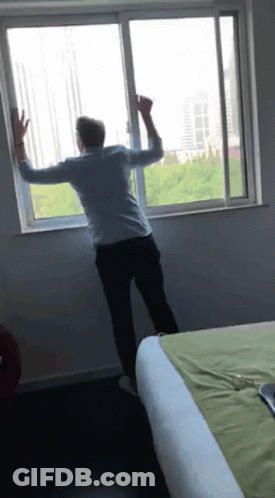 A Man Is Standing In Front Of A Sliding Glass Window GIF