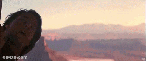A Man Is Standing In Front Of A Sunset Over A Canyon . GIF