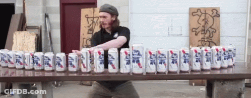 A Man Is Standing In Front Of A Table Full Of Cans Of Beer GIF