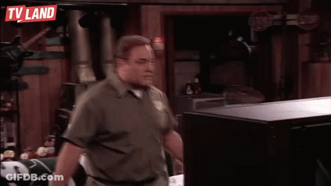 A Man Is Standing In Front Of A Television In A Room With A Tv Land Sign Above Him . GIF