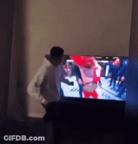 A Man Is Standing In Front Of A Television With A Blurry Picture Of People On It GIF