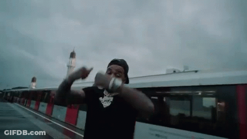 A Man Is Standing In Front Of A Train Holding A Bottle Of Water . GIF