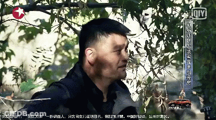 A Man Is Standing In Front Of A Tree With Chinese Writing On The Bottom Right GIF