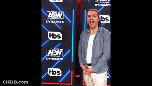 A Man Is Standing In Front Of A Wall That Says Aew GIF