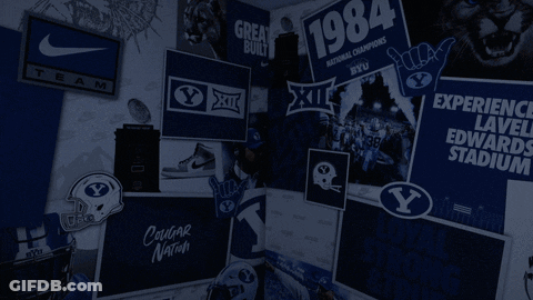 A Man Is Standing In Front Of A Wall With A Sign That Says Experience Lavelle Edwards Stadium GIF