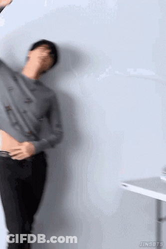 A Man Is Standing In Front Of A Wall With His Shirt Off And Holding His Stomach . GIF