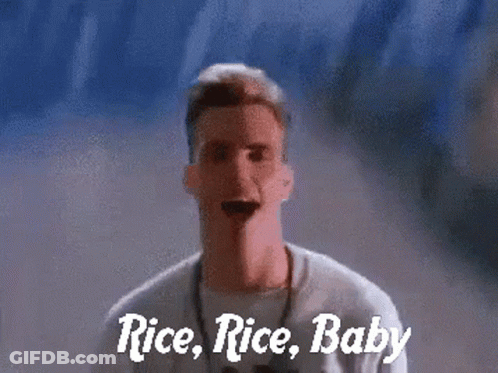 A Man Is Standing In Front Of A Wall With The Words Rice Rice Baby Written On It GIF