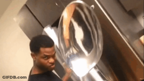 A Man Is Standing In Front Of A Washing Machine And Looking At The Reflection Of Himself In The Mirror . GIF