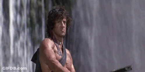 A Man Is Standing In Front Of A Waterfall With His Arms Crossed . GIF