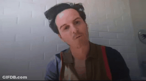 A Man Is Standing In Front Of A White Brick Wall Looking At The Camera . GIF