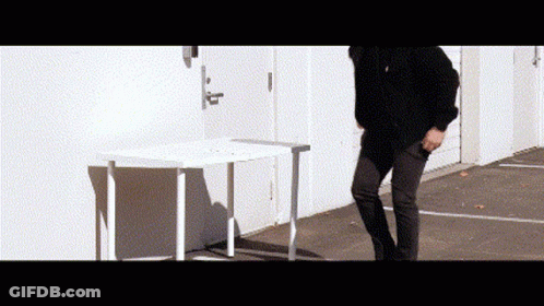 A Man Is Standing In Front Of A White Table . GIF