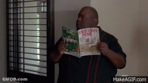 A Man Is Standing In Front Of A Window Holding A Book Titled Traditional Home . GIF