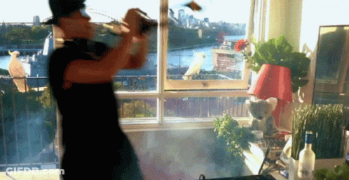 A Man Is Standing In Front Of A Window Holding A Bottle GIF