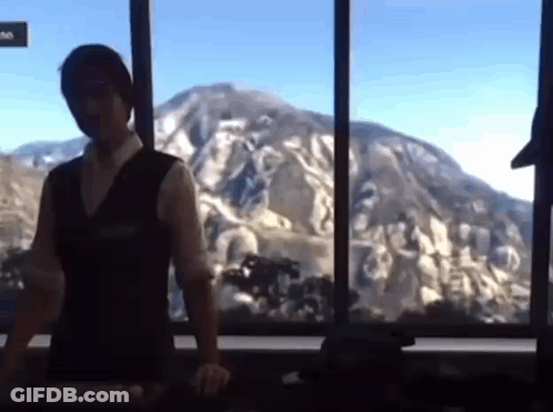 A Man Is Standing In Front Of A Window With A Mountain In The Background GIF