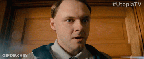 A Man Is Standing In Front Of A Wooden Door With # Utopiatv Written Above Him GIF