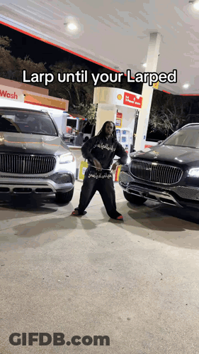 A Man Is Standing In Front Of Two Cars At A Gas Station With A Caption That Says Larp Until Your Larped GIF