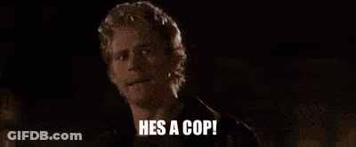 A Man Is Standing In The Dark With The Words `` He 'S A Cop '' Written On His Face . GIF