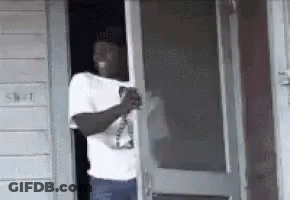 A Man Is Standing In The Doorway Of A Building Holding A Bottle Of Beer . GIF