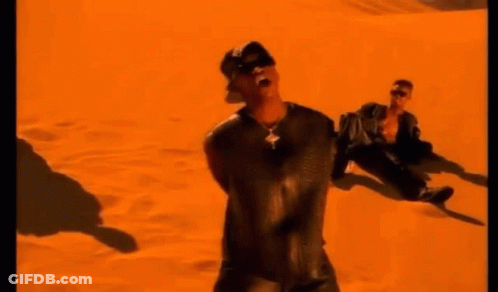 A Man Is Standing In The Middle Of A Desert In Front Of An Orange Background . GIF