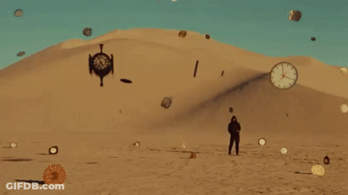 A Man Is Standing In The Middle Of A Desert With Clocks Flying Around Him . GIF