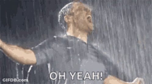 A Man Is Standing In The Rain With His Arms Outstretched And Says Oh Yeah ! GIF