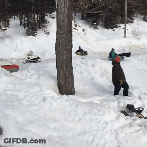 A Man Is Standing In The Snow Near A Tree GIF