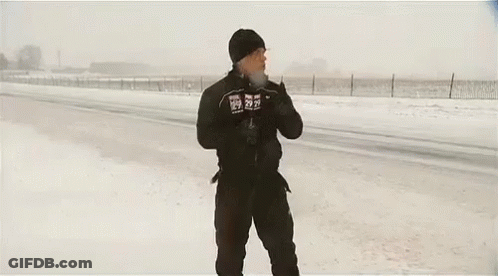 A Man Is Standing In The Snow With His Arms Outstretched In Front Of A Large Truck . GIF