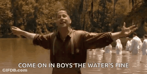 A Man Is Standing In The Water With His Arms Outstretched And A Group Of People Are Standing In The Water . GIF