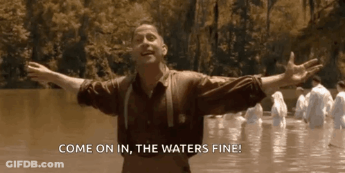 A Man Is Standing In The Water With His Arms Outstretched And A Group Of People Are Standing In The Water . GIF