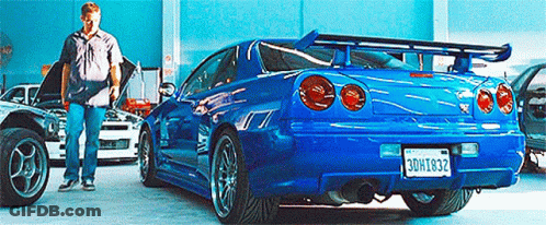 A Man Is Standing Next To A Blue Car With A License Plate That Says Bdh1832 . GIF
