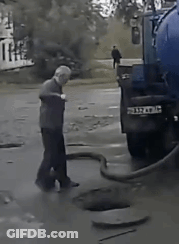 A Man Is Standing Next To A Blue Truck That Is Pumping Water Into A Manhole . GIF