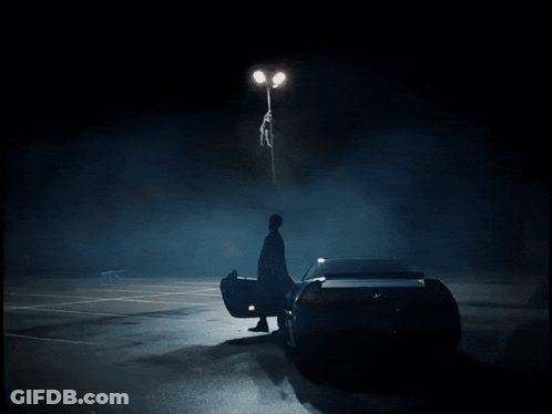 A Man Is Standing Next To A Car In A Dark Parking Lot GIF