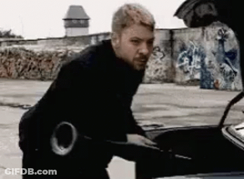 A Man Is Standing Next To A Car With The Hood Open . GIF