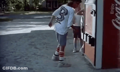 A Man Is Standing Next To A Coca Cola Vending Machine On The Sidewalk . GIF