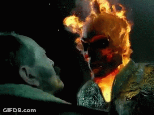 A Man Is Standing Next To A Ghost Rider With Flames Coming Out Of His Face . GIF