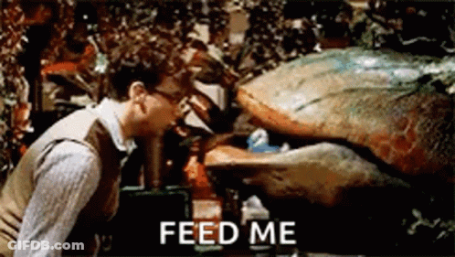 A Man Is Standing Next To A Monster That Says `` Feed Me '' On The Screen . GIF