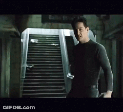 A Man Is Standing Next To A Set Of Stairs In A Dark Room . GIF