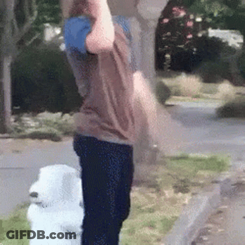 A Man Is Standing Next To A White Dog On The Sidewalk . GIF