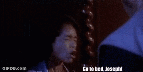 A Man Is Standing Next To A Woman In A Dark Room And Says `` Go To Bed , Joseph '' . GIF